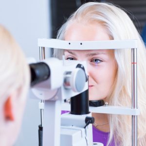 optometry concept - pretty, young female patient having her eyes examined by an eye doctor (color toned image; shallow DOF)